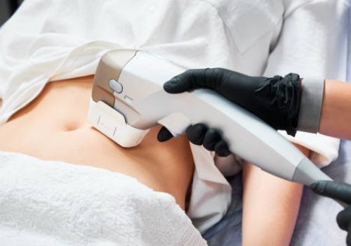 Close up doctor cosmetologist using ultrasound device while performing lifting procedure on woman abdomen. Female patient receiving body tightening and contouring procedure in cosmetology clinic.